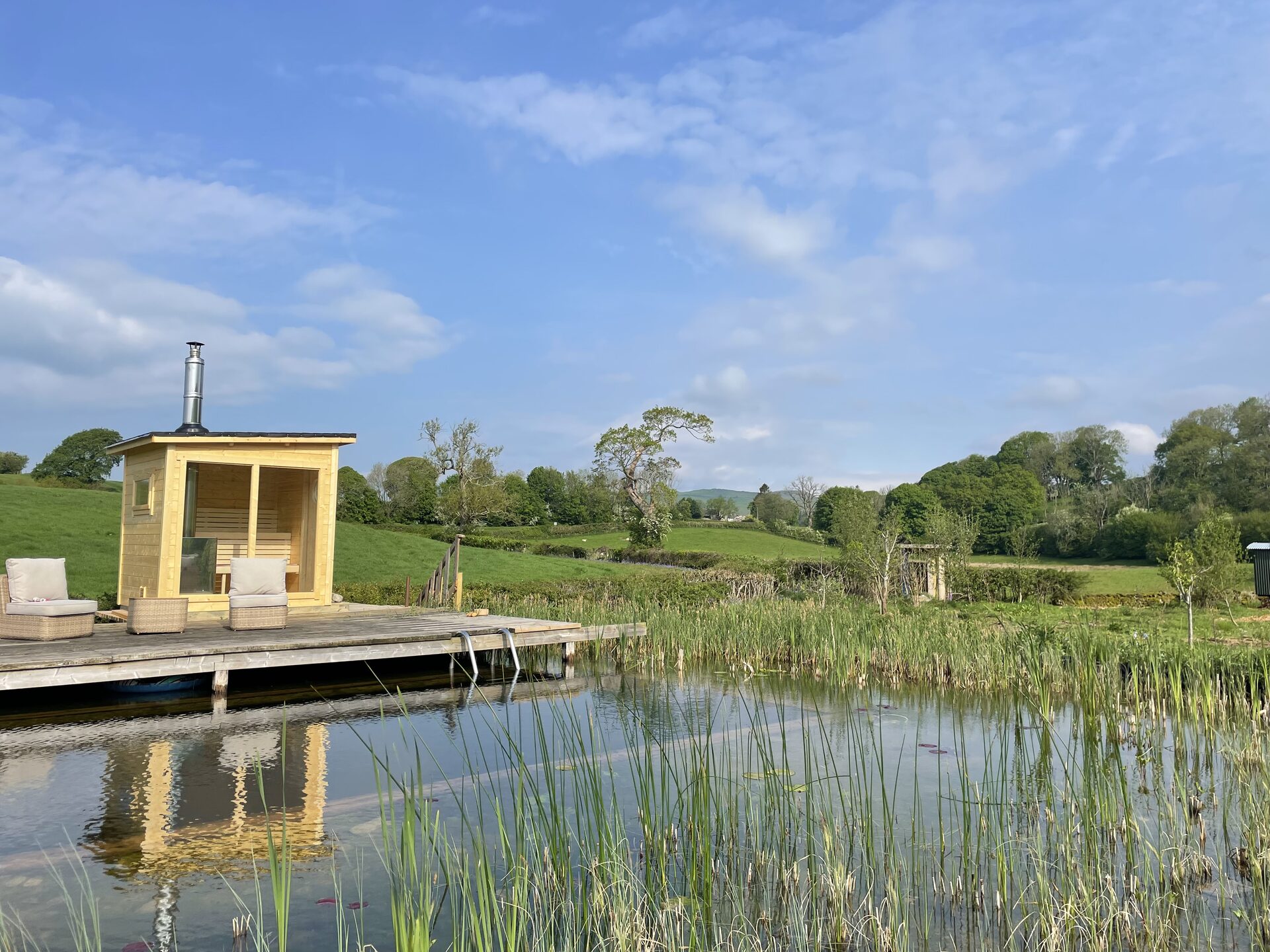 Woodfired cedar sauna on a wooden deck beside a natural swimming pond at Dolly the Hut, Lake District