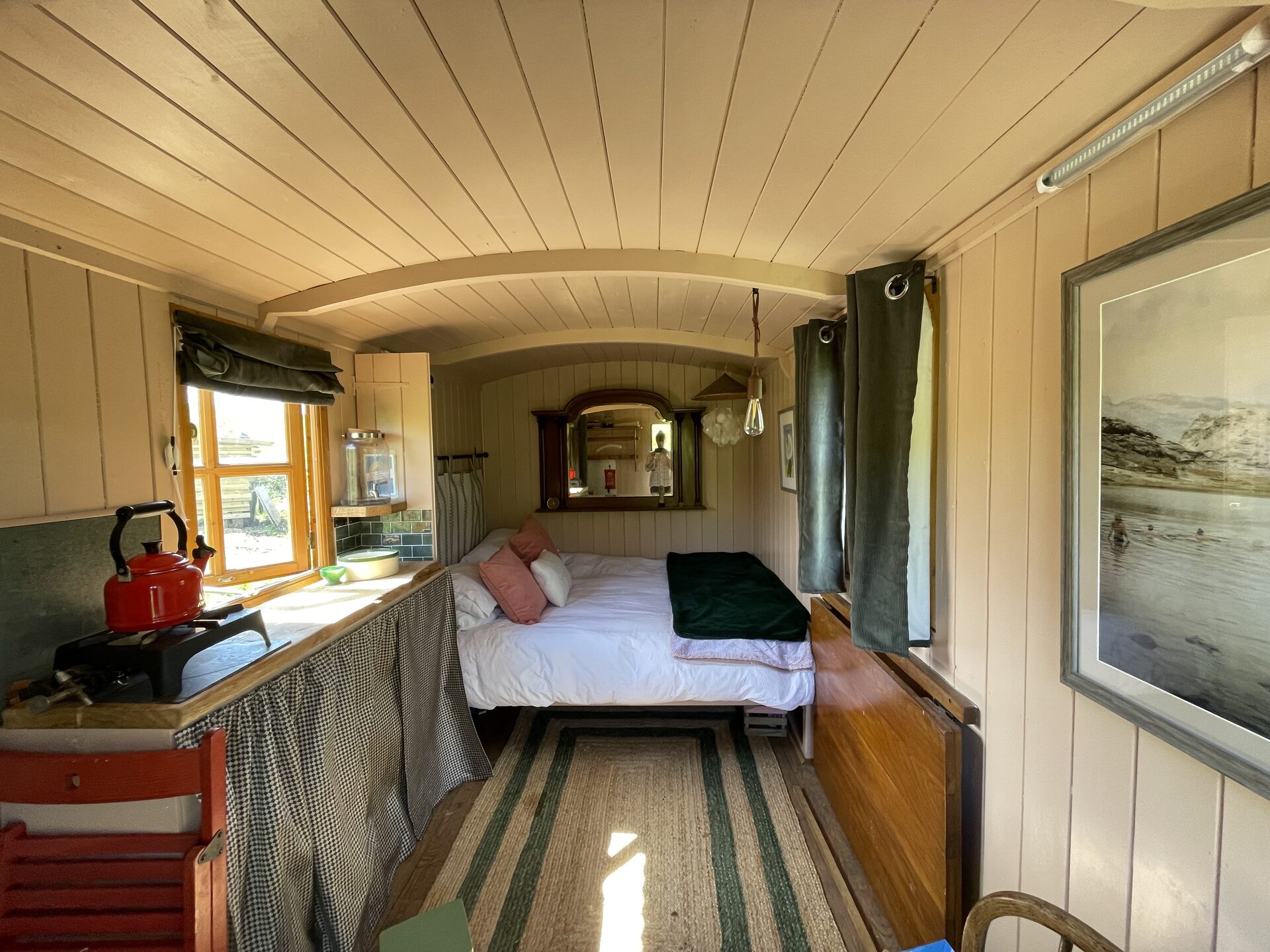 Cosy shepherd's hut interior with double bed, red kettle and Edison bulb