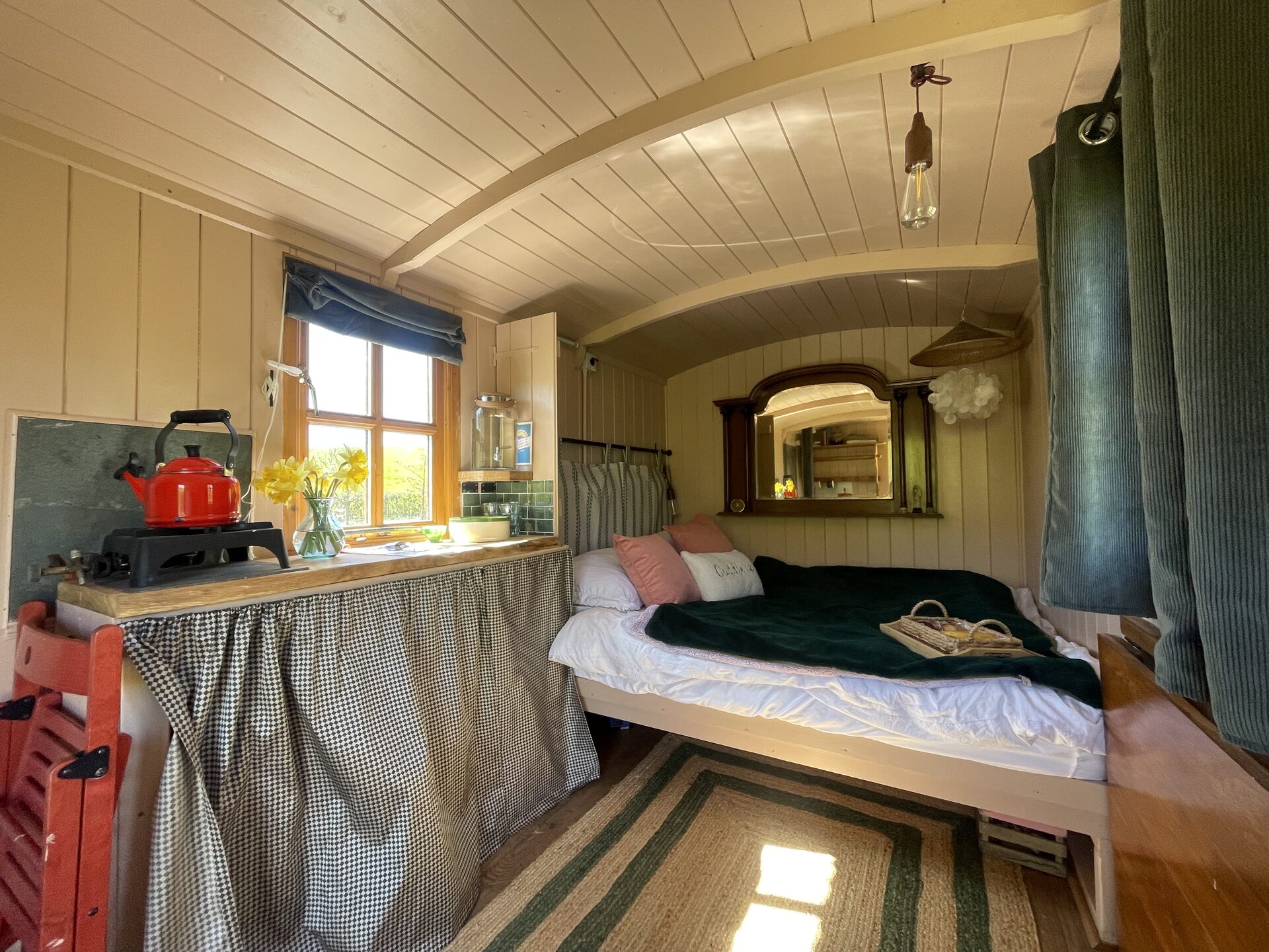 Full view of the cosy shepherd's hut interior with double bed, red kettle and arched ceiling