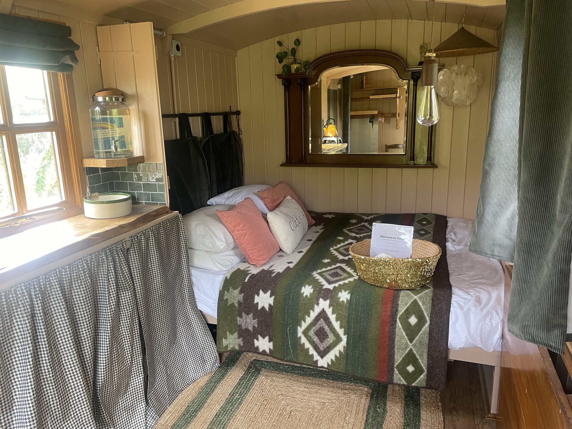 Shepherd's hut interior with the double bed made up with a wool blanket, cushions and a welcome basket