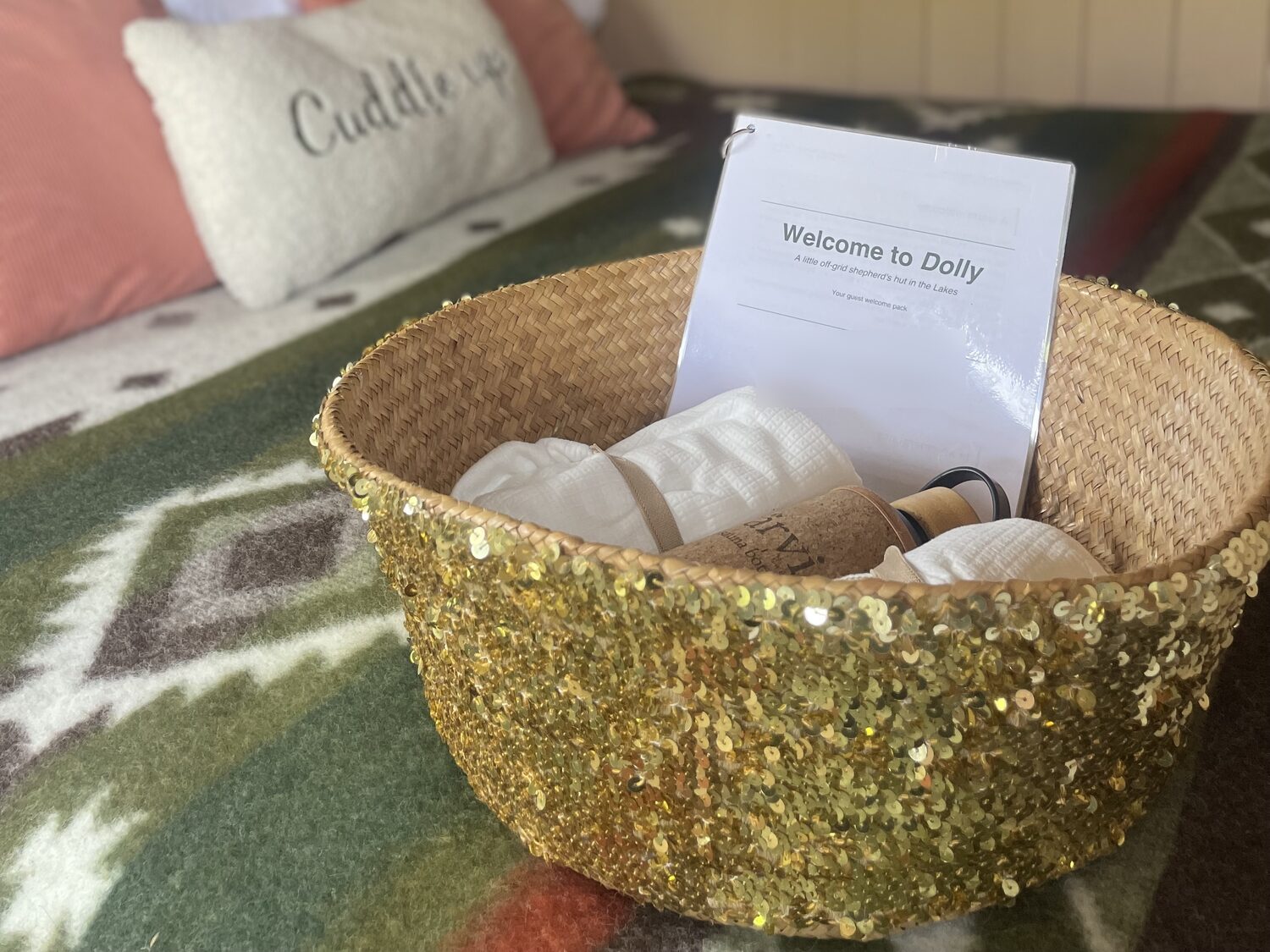Gold sequinned welcome basket on the bed with rolled towels and the guest welcome pack
